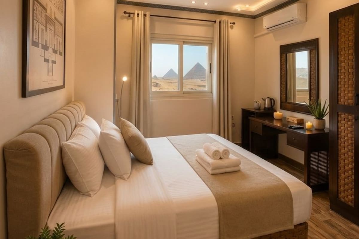 Habitación de hotel con una cama grande, un escritorio, un ventanal con vistas a las pirámides y un aire acondicionado instalado en la pared.