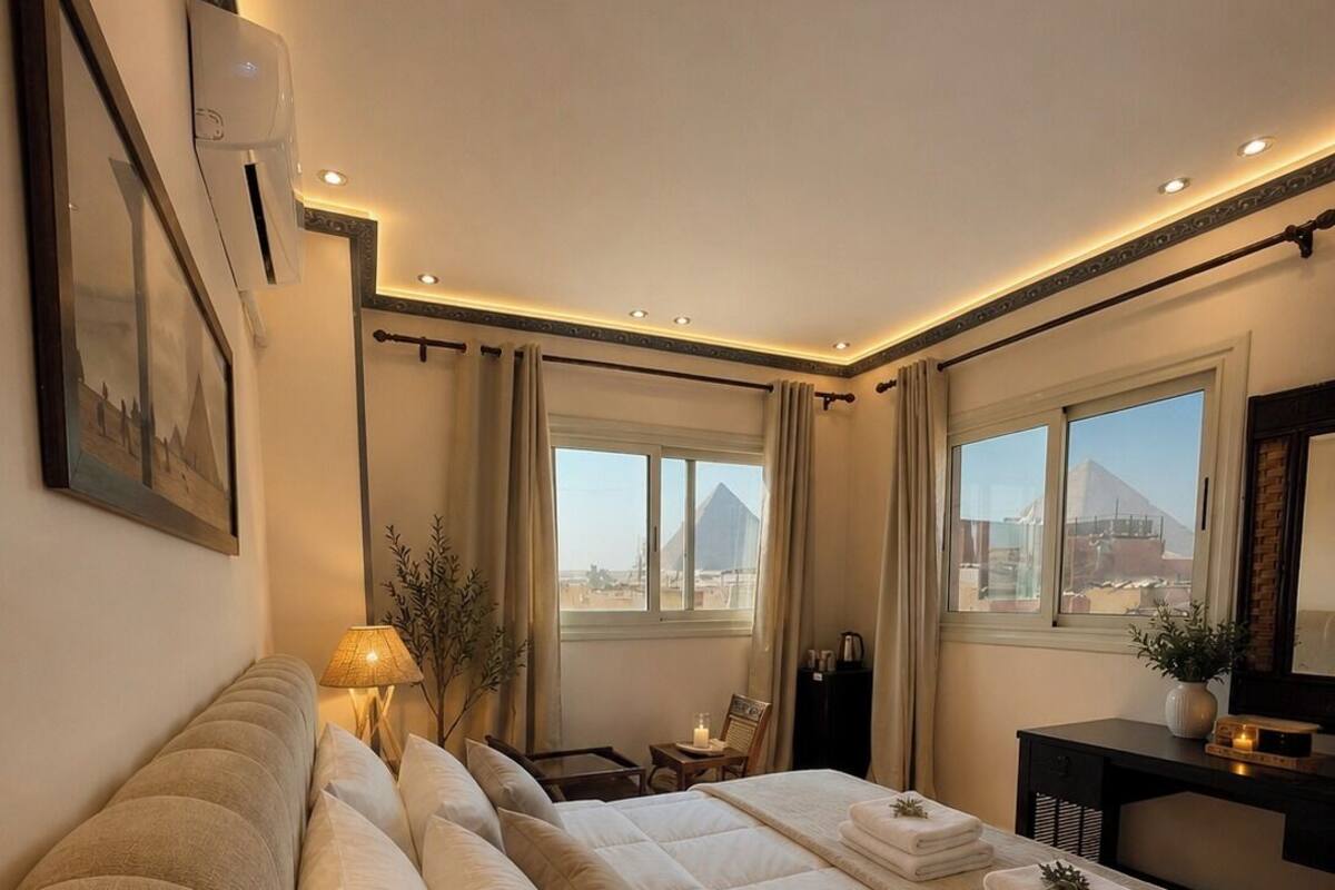 Habitació d'hotel amb un llit gran, una taula, una cadira, una làmpada i vista a una piràmide.