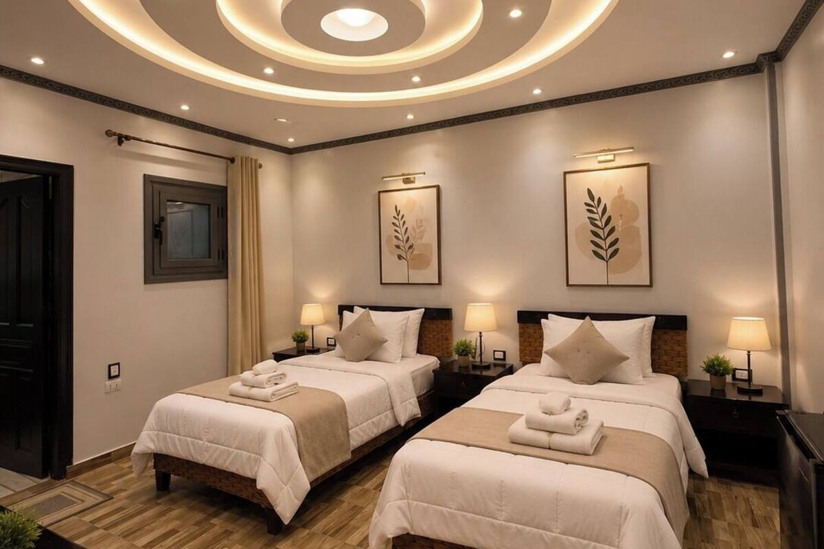 Habitació d'hotel amb dos llits, una làmpada de sostre de disseny circular i un paviment de fusta.