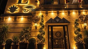 A hotel with a prominent illuminated sign, a grand entrance with a decorative door, and flags displayed outside. - Foola Pyramids Inn Hotel (Giza)