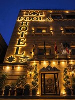 Un hotel con un llamativo letrero iluminado, una entrada imponente con una puerta decorativa y banderas visibles en el exterior.