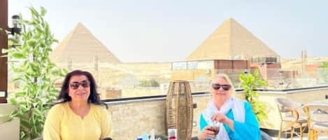 Deux personnes sont assises à une table en plein air, d’où l’on peut admirer les pyramides.