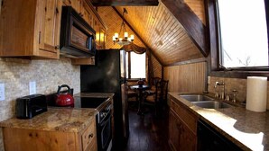 Una cocina con armarios de madera, estufa, lavaplatos y una araña.