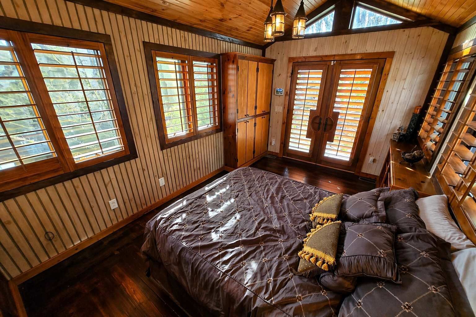 Une chambre à coucher avec un grand lit, des murs en bois et de nombreuses fenêtres.