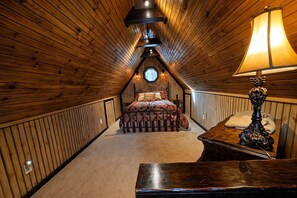 Ein gemütliches Schlafzimmer im Dachgeschoss mit schrägen Wänden, einem Bett mit Blumenmuster, einer Lampe und einem kleinen Tisch.