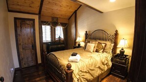 Un dormitorio con un cabecero de madera, dos mesitas de noche con lámparas, un aparador y una puerta.