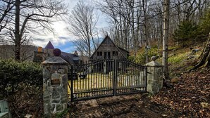 A gated entrance to a rustic cabin with a stone gate, surrounded by trees and a dirt path. - Pet-Friendly Chateau with Hot Tub (Sugar Mountain)