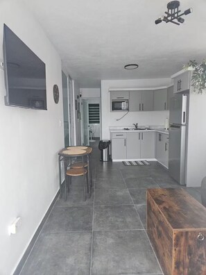 A modern kitchen with grey cabinets, a microwave, and a refrigerator. There is a dining area with a table and chairs.