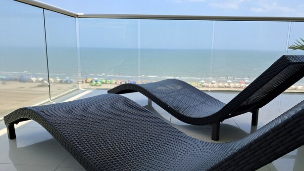 En balkon med to sorte fletstol, der vender ud mod en strand.