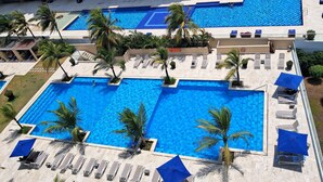 En stor udendørs swimmingpool med flere baner, omgivet af palmer og liggestole.