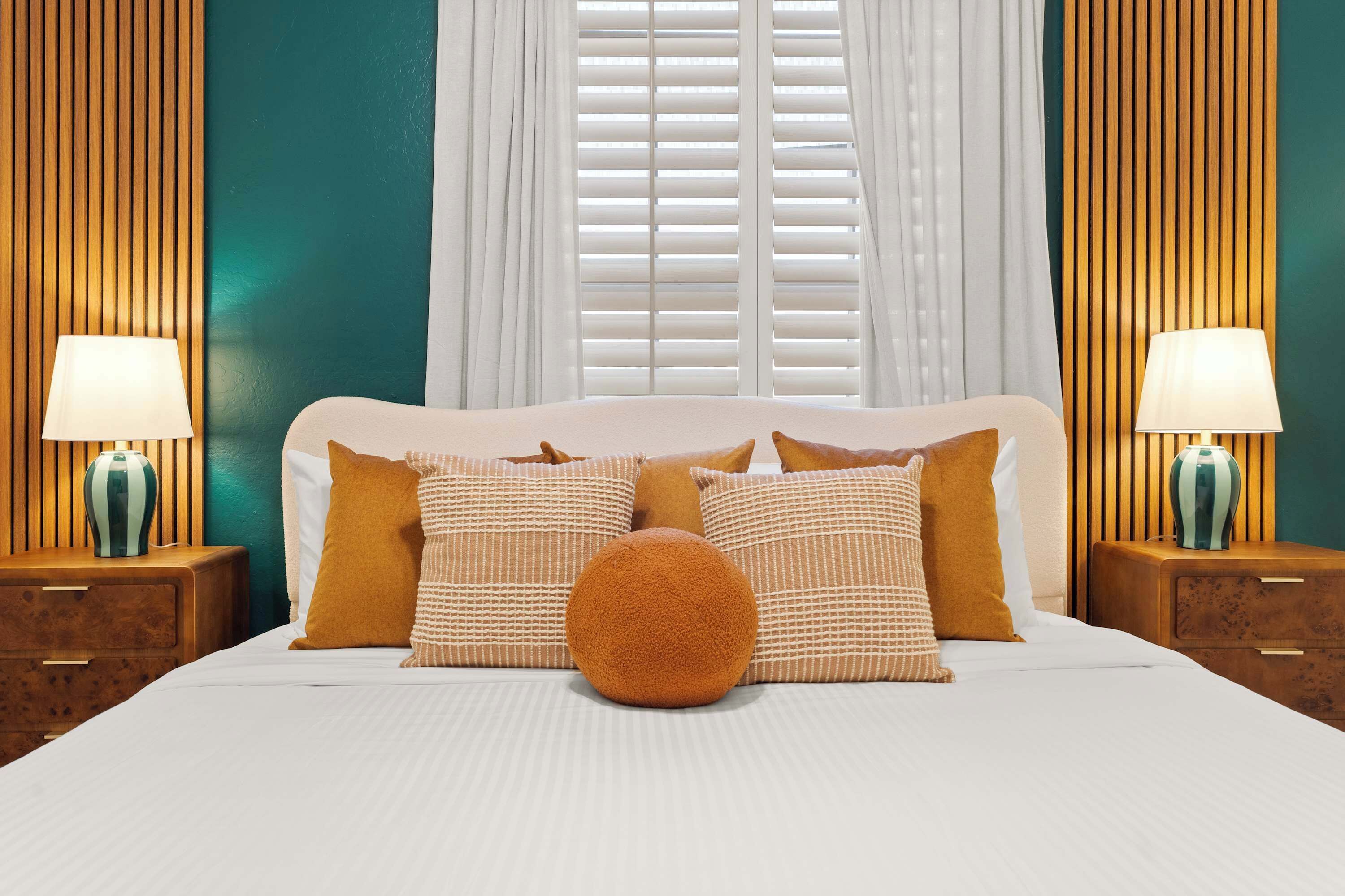 A neatly made bed with a white headboard, two bedside tables with lamps, and a window with blinds.