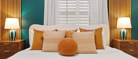 A neatly made bed with a white headboard, two bedside tables with lamps, and a window with blinds.