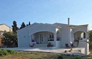 Ein weißes Gebäude mit einer überdachten Veranda, Sitzgelegenheiten im Freien und Blumentöpfen.