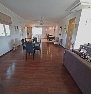 Ein geräumiger Wohnbereich mit Esstisch, Stühlen, einer Couch und einer Küche im Hintergrund.