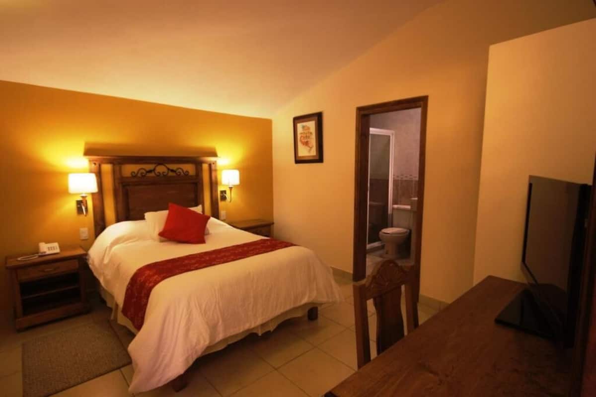 A hotel room with a bed, bedside lamps, a television, a desk, and a bathroom door.