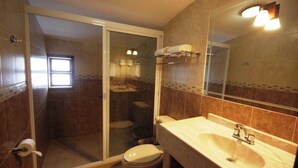 Ein Badezimmer mit einer Duschkabine, Toilette, Waschbecken und einem Spiegel.
