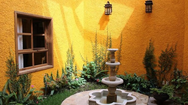 Ein Innenhof mit einem Brunnen, einem Fenster und Kübelpflanzen an einer gelben Wand.