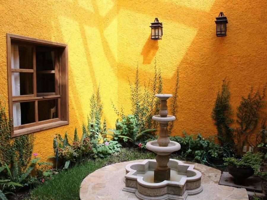 Pátio com uma fonte, janela e vasos de plantas em frente a uma parede amarela.