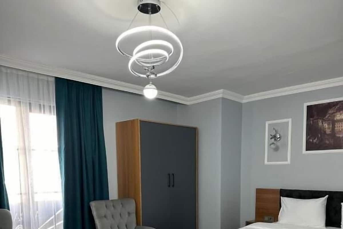 Ein Hotelzimmer mit einem Bett, zwei Sesseln, einem kleinen Tisch, einem grünen Teppich, einem Kleiderschrank und einer Deckenleuchte.