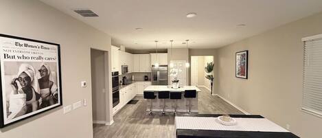 A modern kitchen with a central island, bar stools, and a dining table with a placemat.