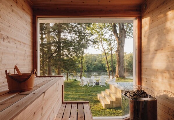 A wooden cabin with a view of a river and chairs outside.
