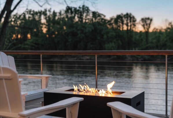 A deck with a fire feature, chairs, and a view of a body of water.