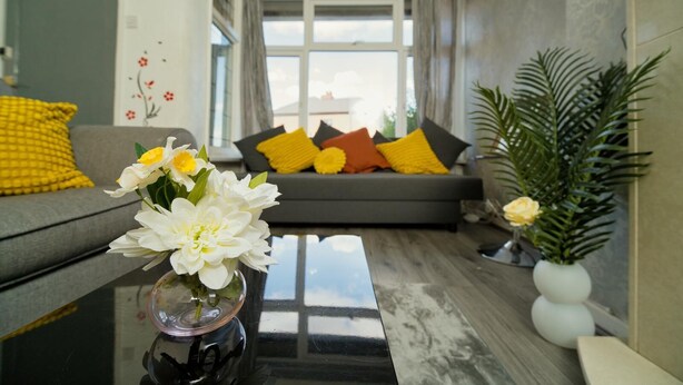 Een moderne woonkamer met een bank, kussens, een vaas met bloemen en een potplant.