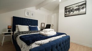 Een slaapkamer met een groot bed, een nachtkastje met een lamp, een stoel en een ingelijst schilderij aan de muur.