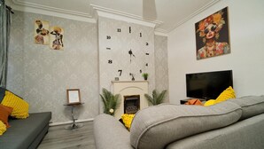 Een woonkamer met een open haard, een bank, een televisie en decoratieve muurkunst.