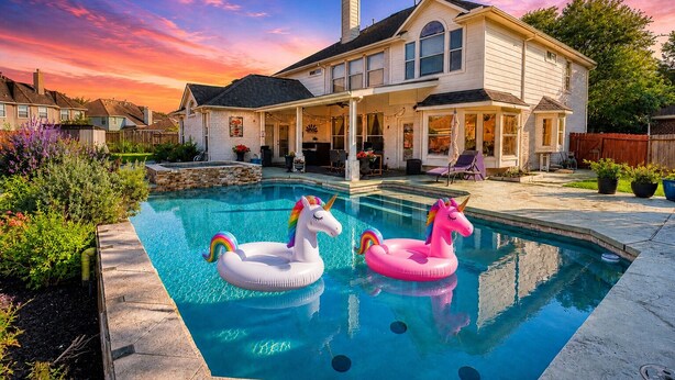 Ein Wohnhaus mit Schwimmbad, zwei aufblasbaren Einhorn-Schwimmfiguren und einer überdachten Terrasse.