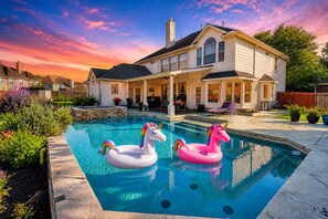 Ein Wohnhaus mit Schwimmbad, zwei aufblasbaren Einhorn-Schwimmfiguren und einer  überdachten Terrasse.