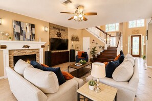 A spacious living room with a fireplace, a large TV, and a staircase leading to another level. - FIFA Traveler's Oasis Pool Sauna Patio Arcade Sleep 14+ (Richmond)