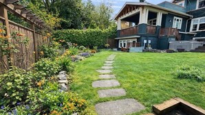 A residential property with a well-maintained lawn, a stone pathway, and a wooden deck. - The Ellery | Garden Suite Historic Queen’s Park (New Westminster)