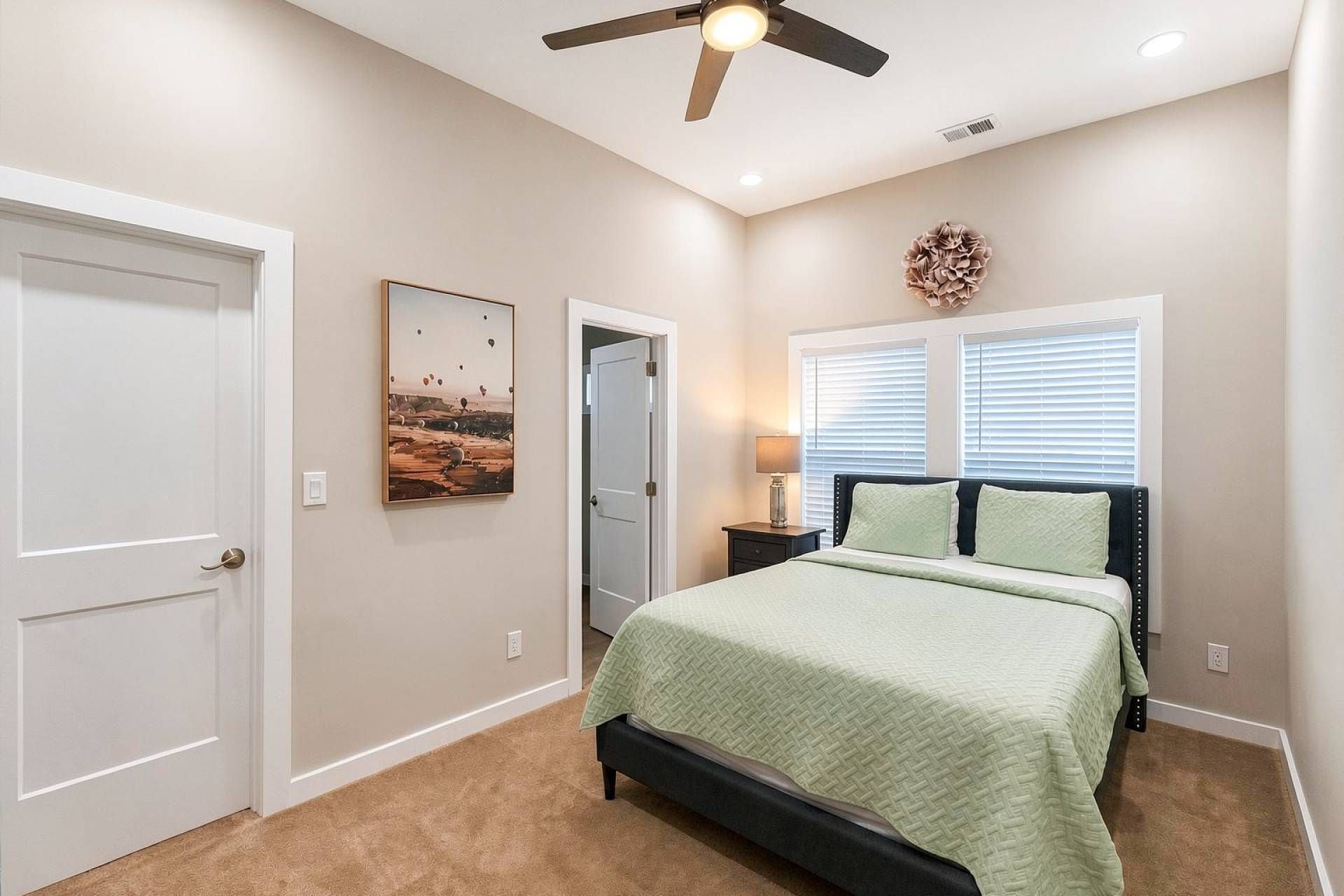 Une chambre à coucher avec un lit, un ventilateur de plafond, une fenêtre avec des stores et une porte.