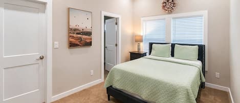 Une chambre à coucher avec un lit, un ventilateur de plafond, une fenêtre avec des stores et une porte.