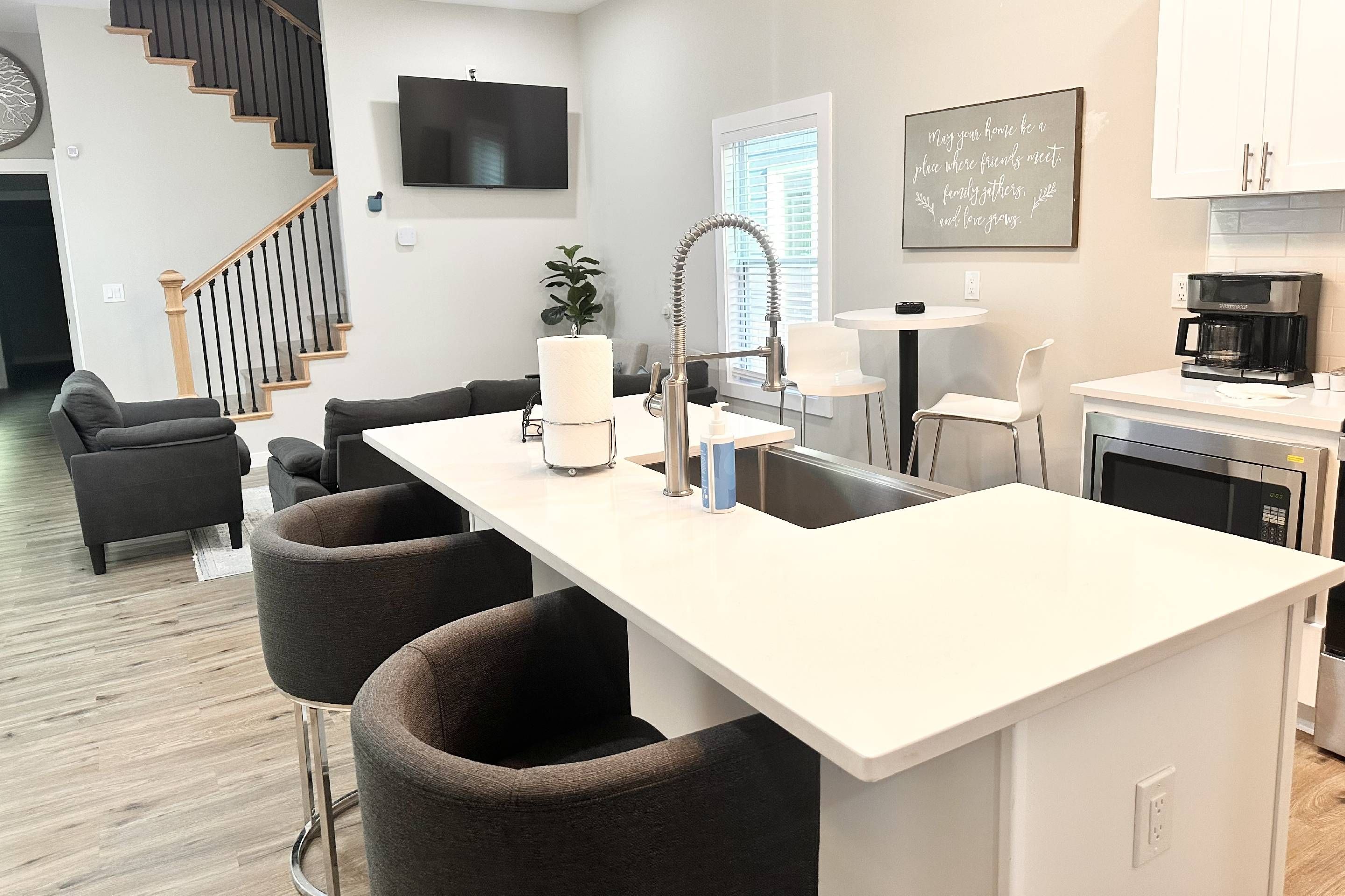A modern kitchen with a central island, bar stools, a coffee machine, and a dining area with a table and chairs.