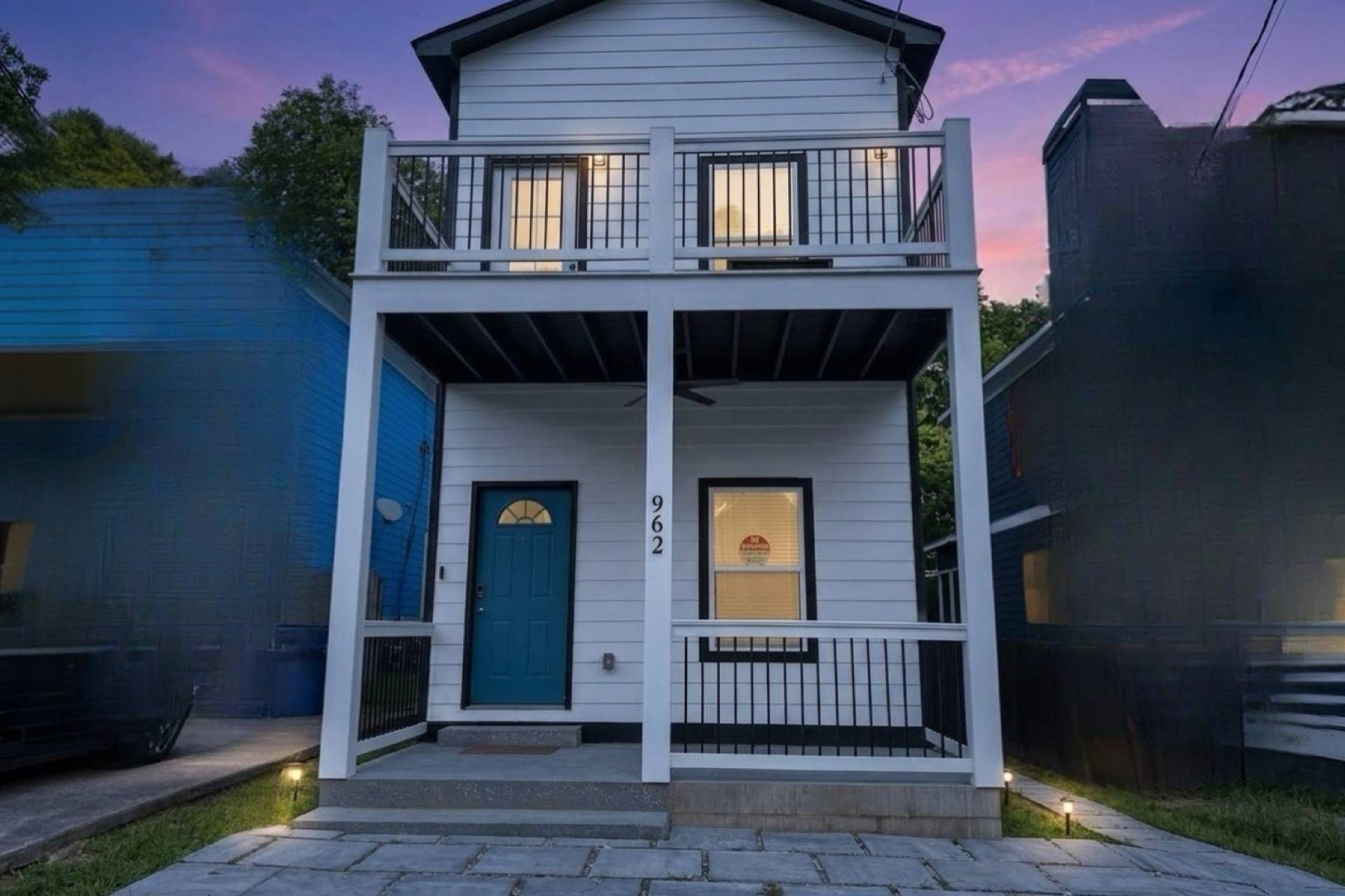 Una casa de dos pisos con una puerta azul, un balcón y el número 962 en la fachada.