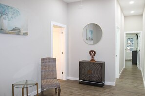 A hallway with a wicker chair, a glass table, a dark console with a mirror, and a painting on the wall. - New -Atlanta Gem-Close to Mercedes-Benz (World Cup), World Congress Center & State Farm (Atlanta)