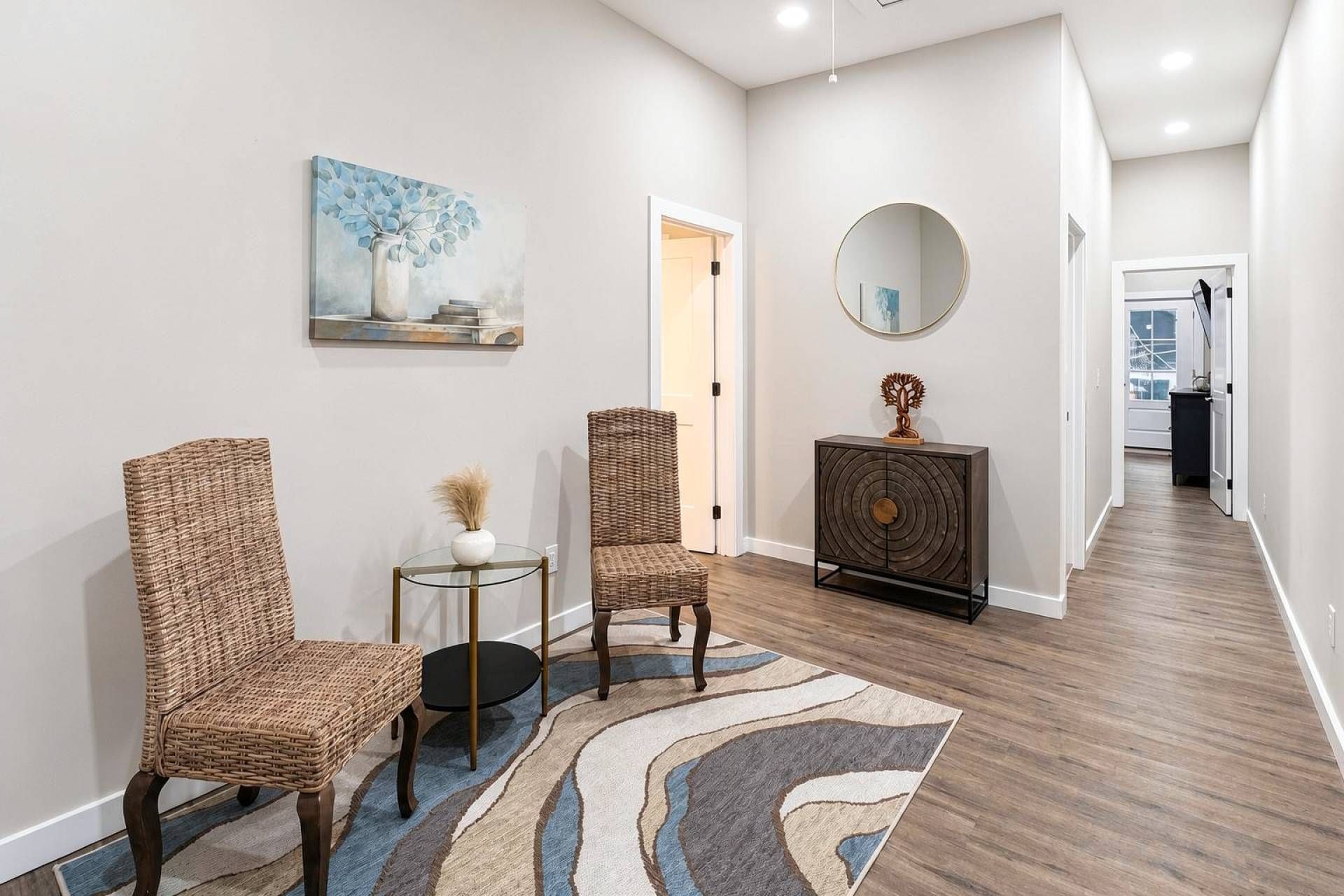 A hallway with two wicker chairs, a small round table, a decorative console, and a painting on the wall.