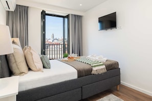 Ein modernes Hotelzimmer mit einem großen Bett, einem an der Wand montierten Fernseher und Blick auf die Stadt durch das Fenster.
