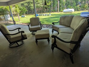 Ein überdachter Patio-Bereich mit einer Eckcouch, zwei Sesseln und einem kleinen Hocker.