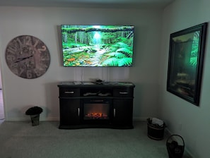Ein Wohnzimmer mit Flachbildfernseher, Kamin, einer Uhr und einem gerahmten Bild an der Wand.