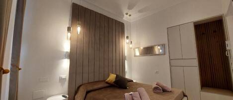 A modern bedroom with a large bed, bedside lamps, a mirror, and a wardrobe.