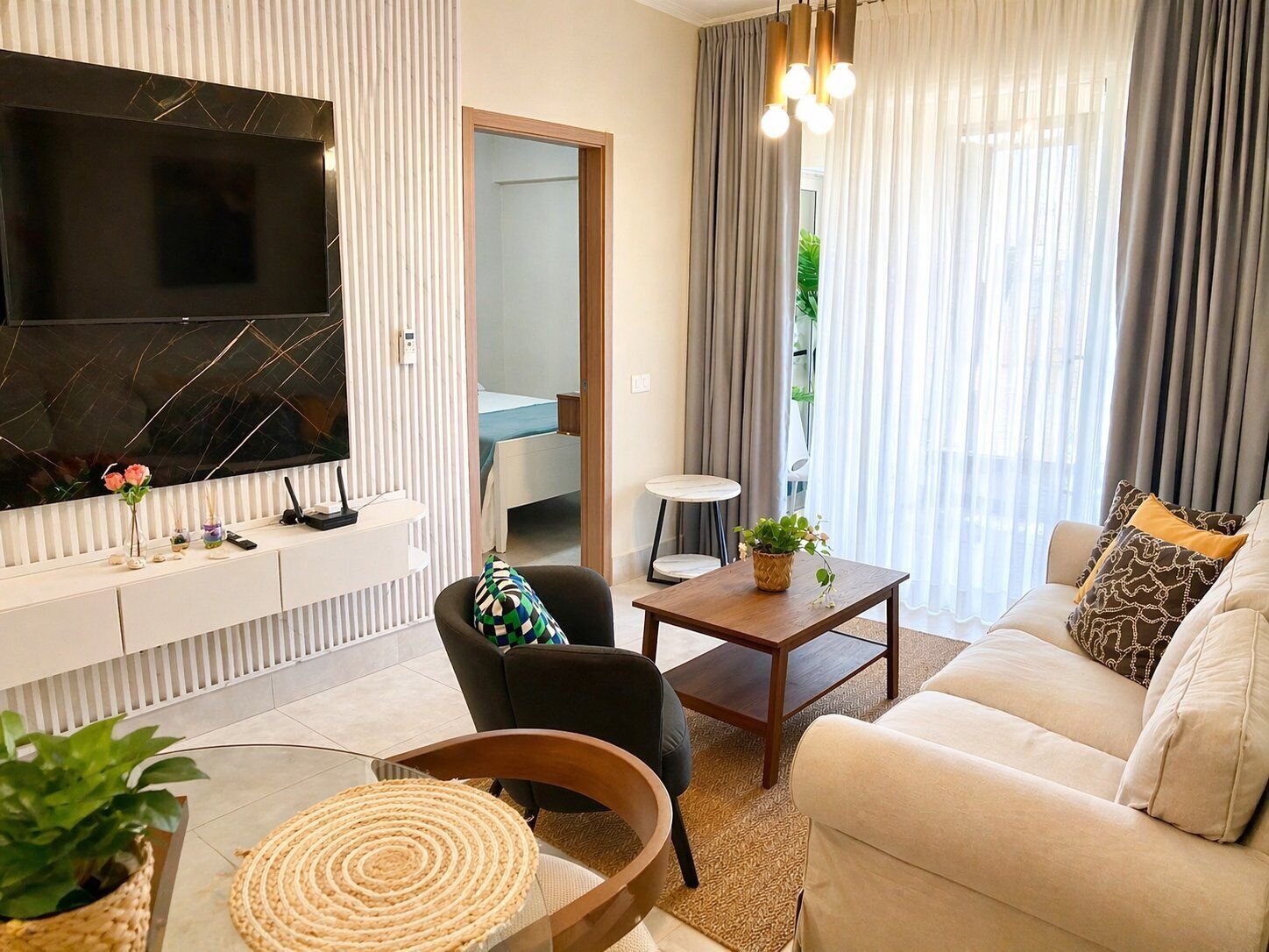 A modern living room with a flat-screen TV, a sofa, a coffee table, and a chair. There is a small table with a plant and a decorative item.