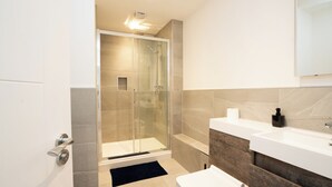Un baño moderno con cabina de ducha de vidrio, un lavabo blanco y un mueble de tocador de madera.