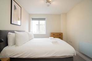 Une chambre à coucher comprenant un lit, une fenêtre, une table de chevet et une œuvre d’art accrochée au mur.