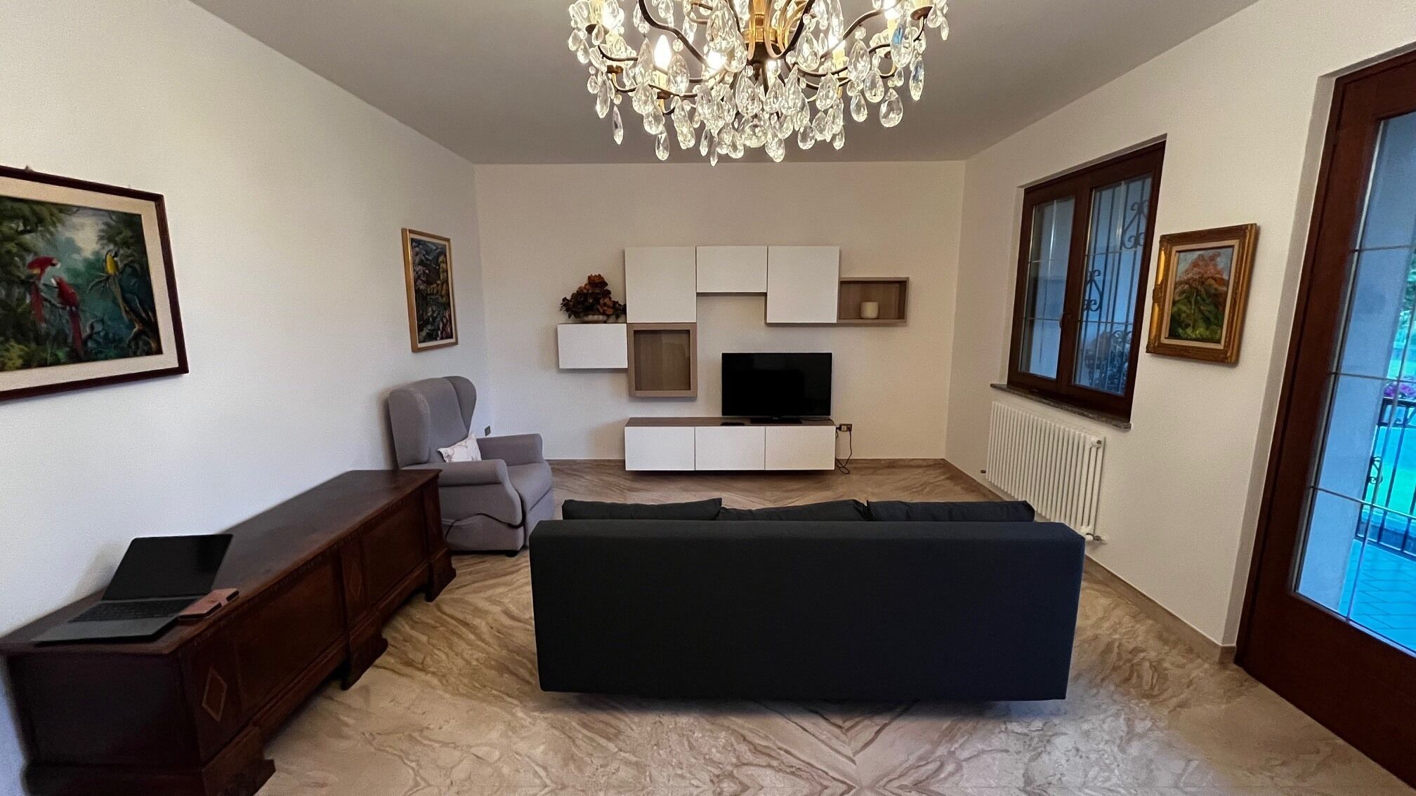 A living room with a sofa, a TV, a chandelier, and artwork on the walls.