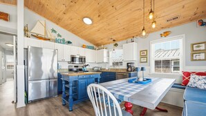 A kitchen with a central island, wooden ceiling, and a dining area with a checkered tablecloth. - MargaritaPhil - Steps from Beach and Pier (Kill Devil Hills)