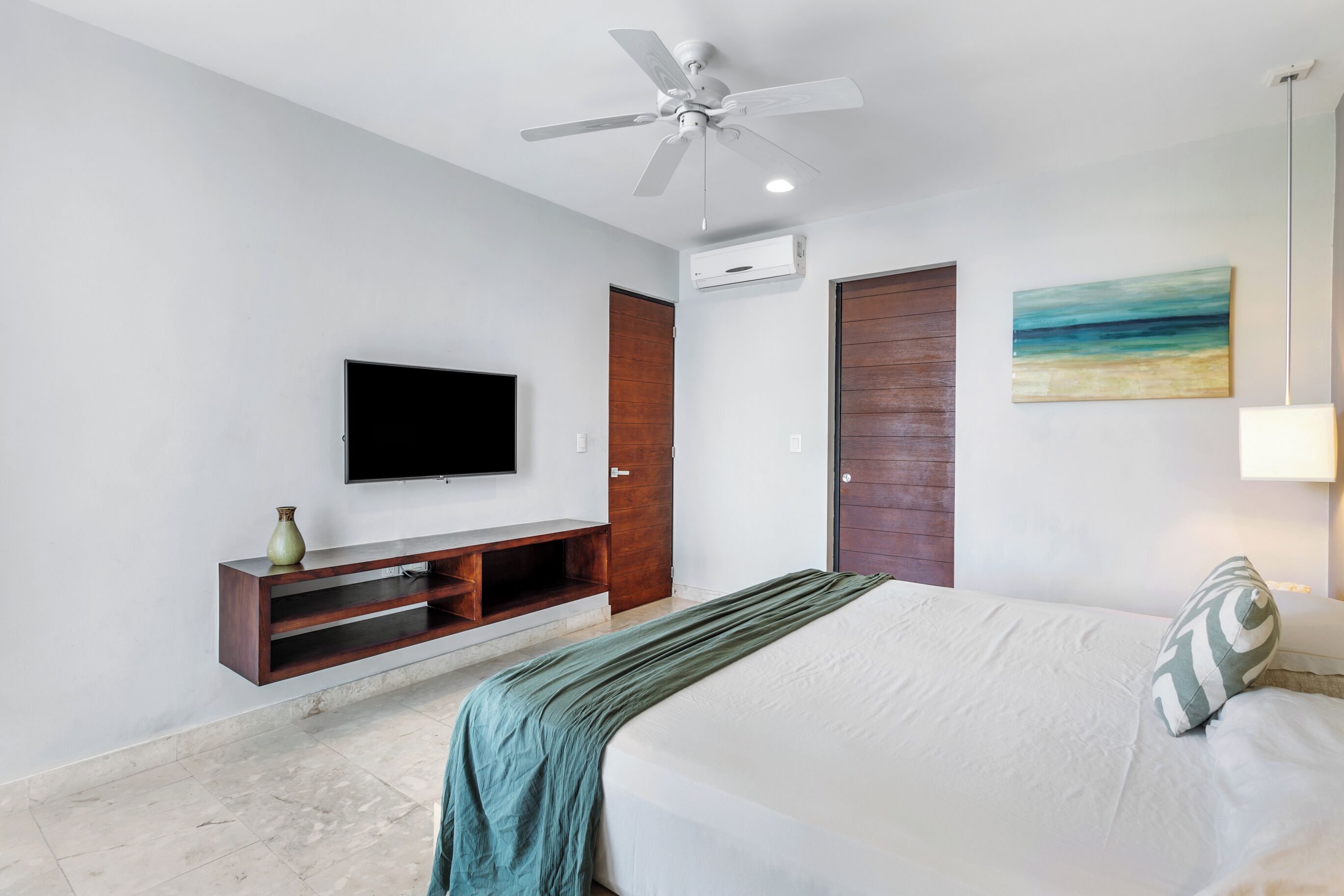 Une chambre à coucher avec un lit, un téléviseur fixé au mur, un ventilateur de plafond et une porte.