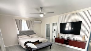 A bedroom with a bed, a bench, a TV, and a ceiling fan. - Bajan Bliss Townhouse ✈️ | 5–10 Min to Airport & Shopping. Modern and Spacious (St Philip)